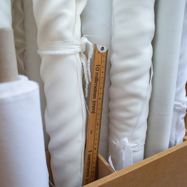Rolls of bridal fabric stood upright with meter rule stored in wooden box in my studio