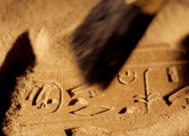 A brush cleaning sand to reveal ancient symbols or hieroglyphs.