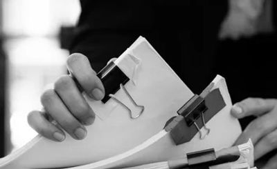 Person organizing multiple stacks of papers with binder clips on a wooden desk.