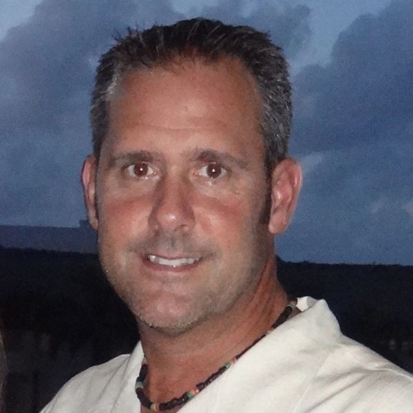 Man smiling outdoors at dusk.