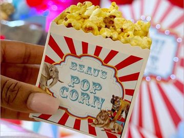Hand holding a vintage-style box of popcorn with circus-themed design.