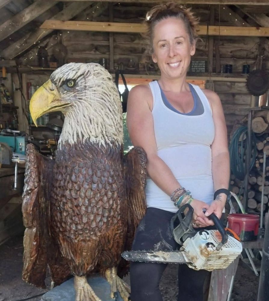 Woman posing with a large wooden eagle sculpture and chainsaw.