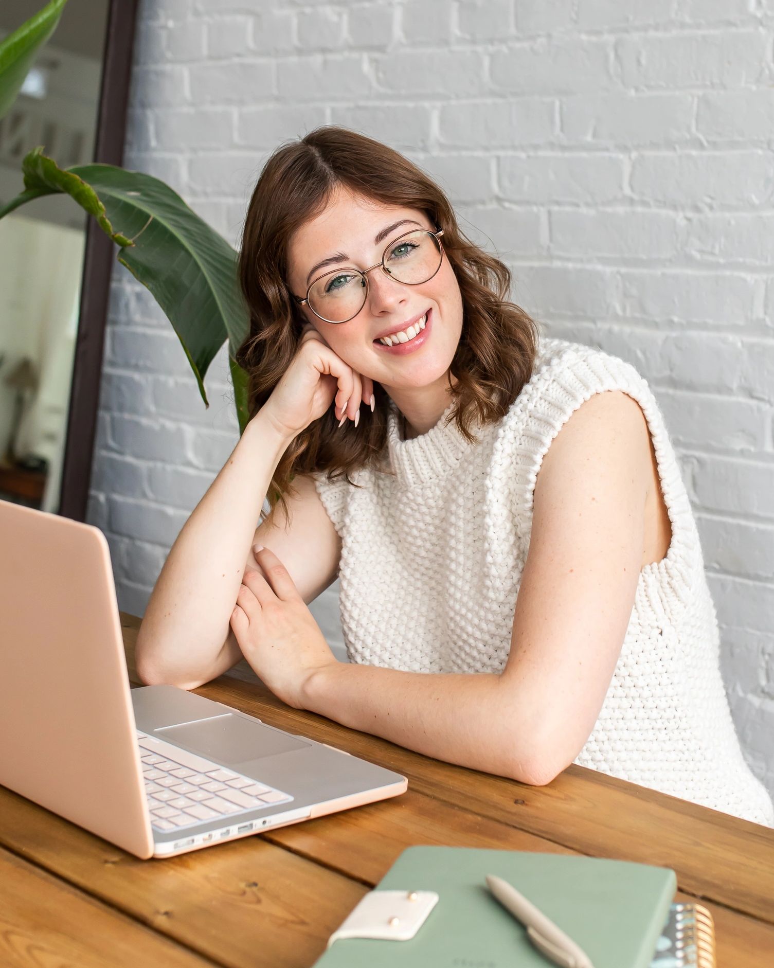 Therapist sitting at a desk with a laptop and notebooks in front, smiling toward the camera.