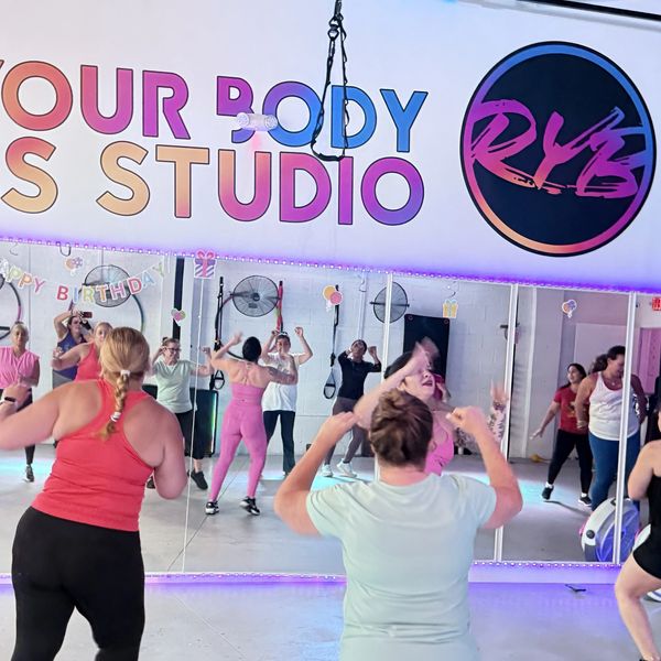 Group fitness class in a colorful, energetic studio with mirrored walls.
