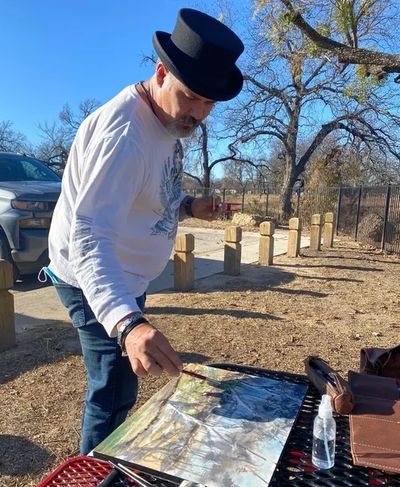 A man in a top hat painting outdoors on a sunny day.