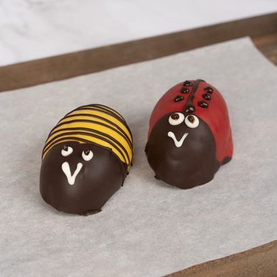 Yellow bumble bee cake and red ladybug cake sitting on top of parchment paper and cutting board.