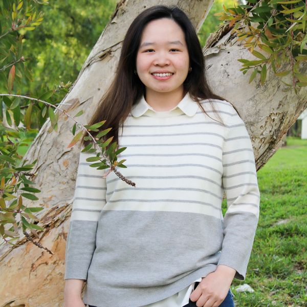 Hilary Ghozali, smiling in casual attire outdoors by a tree
