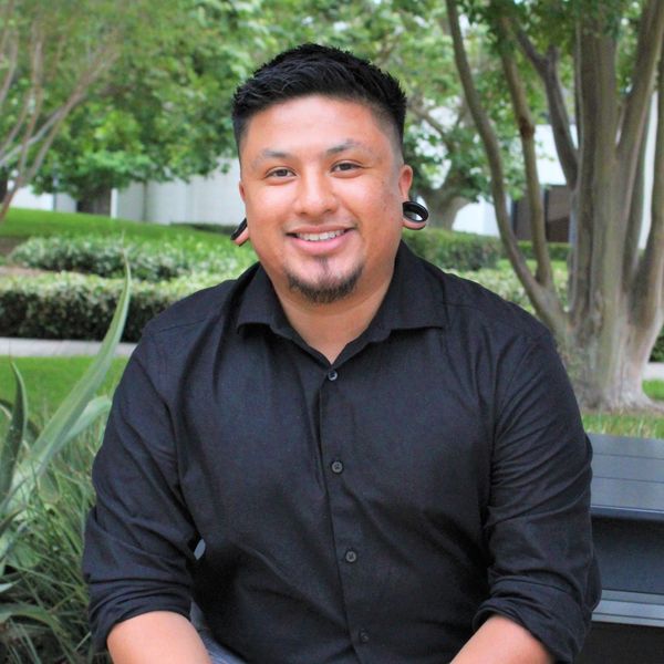 Herbert Hernandez in black shirt and gray pants sitting on a bench outdoors.