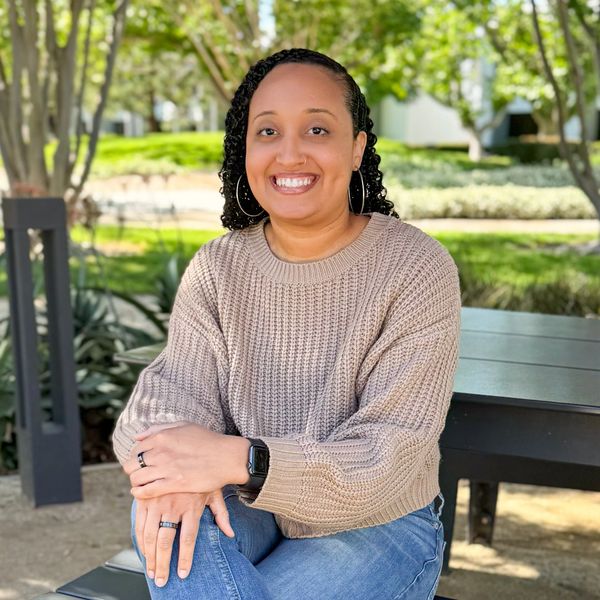 Smiling woman in a cozy sweater sitting outdoors on a bench.