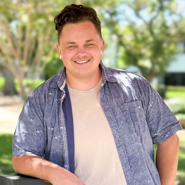 Smiling person leaning on a railing outdoors.