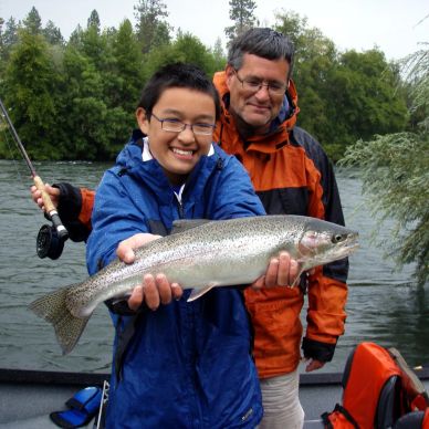 A boy proudly holding a fish he caught while fishing with an older man.
