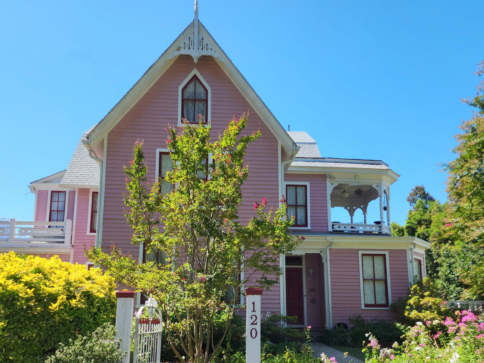A charming pink Victorian house with intricate woodwork and lush garden.