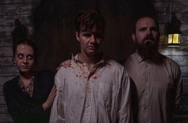 Three eerie figures in dim light, one with blood-stained clothing.