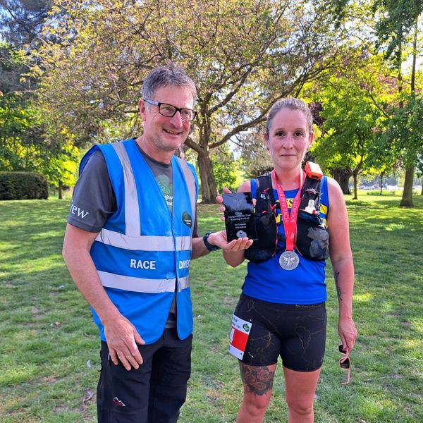 Race director and female runner with award in park.