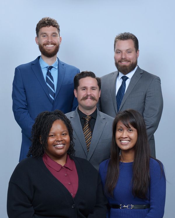 Five professionally dressed individuals posing together, smiling.