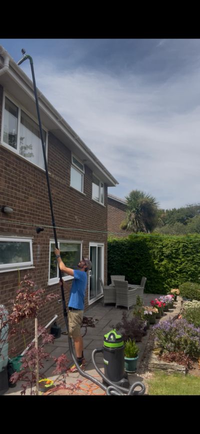 Man cleaning house gutters with a long vacuum tube.