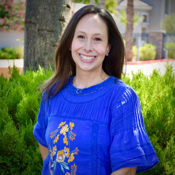 Woman smiling outdoors in a blue floral dress.