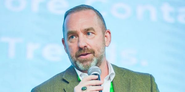 Man in a blazer speaking into a microphone at a conference.
