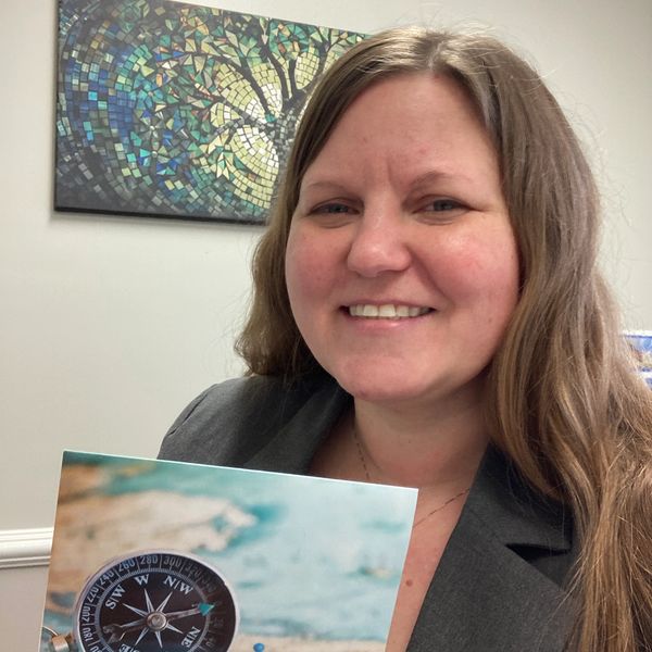 Smiling woman holding a compass-themed picture indoors.