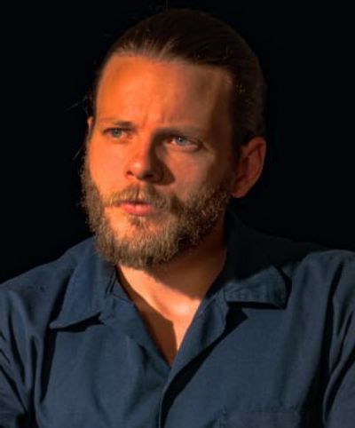 Man with beard in blue shirt under warm light.