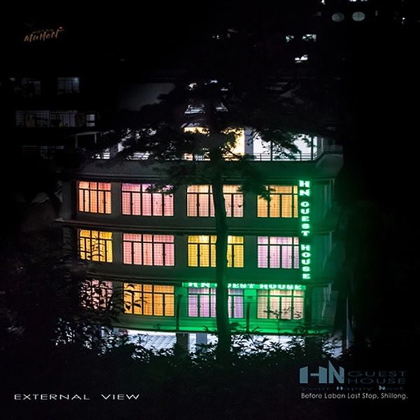 Colorfully lit HN Guest House building at night surrounded by trees.