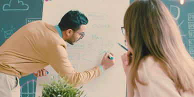 Man explaining ideas on a whiteboard to a woman in a creative workspace.