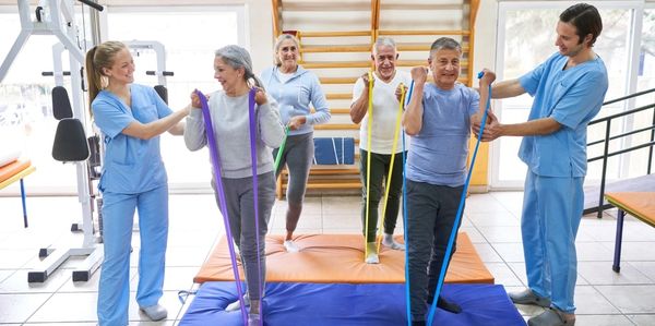 Senior adults exercising with resistance bands guided by healthcare professionals.
