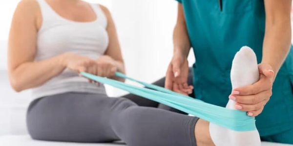 A therapist helps a woman stretch her foot with a resistance band.