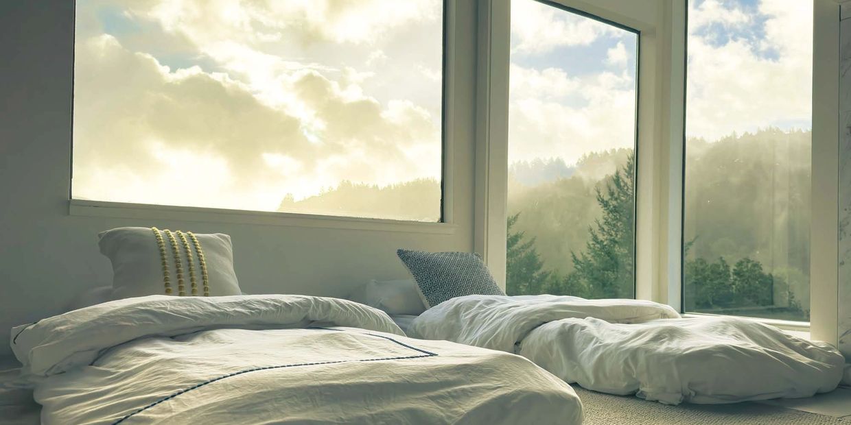 Cozy floor beds with large windows overlooking a misty forest landscape.