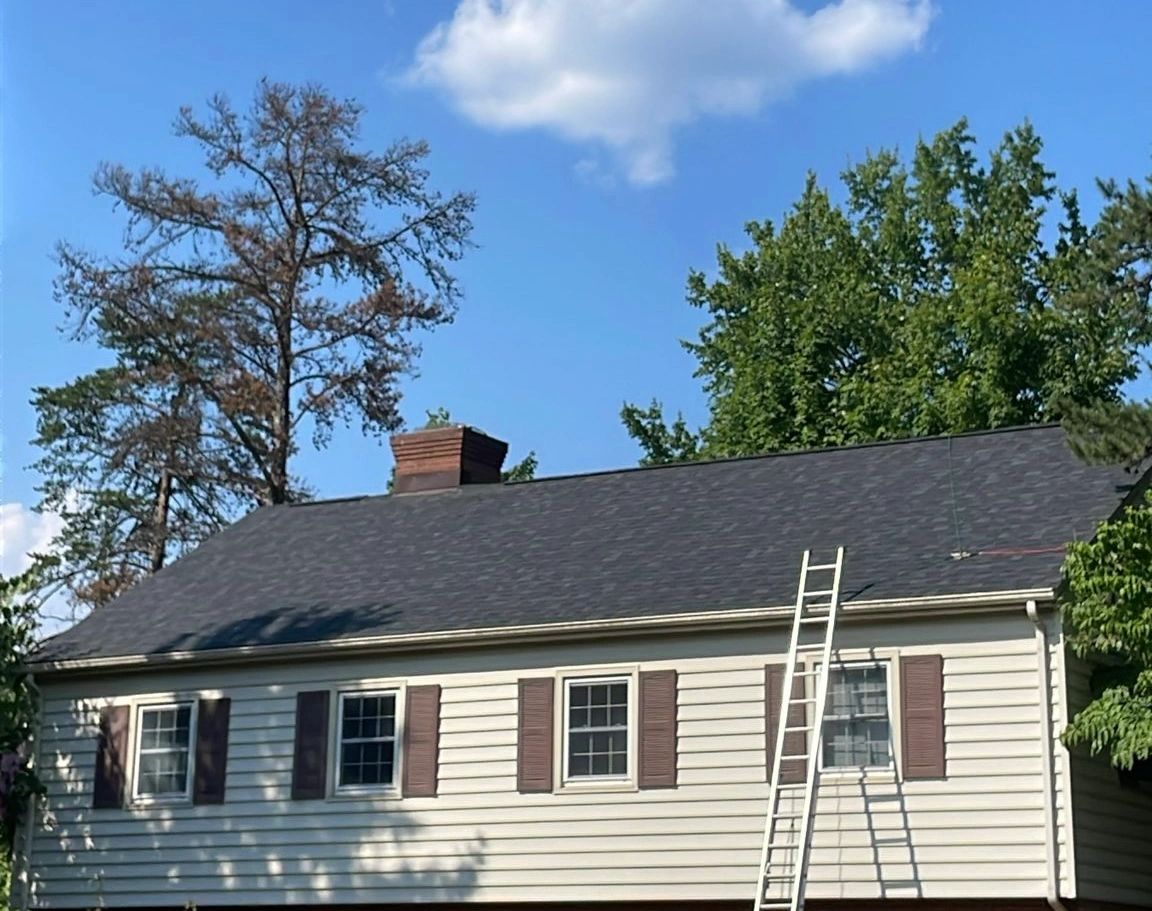 A house with a ladder leaning on its roof under a partly cloudy sky.