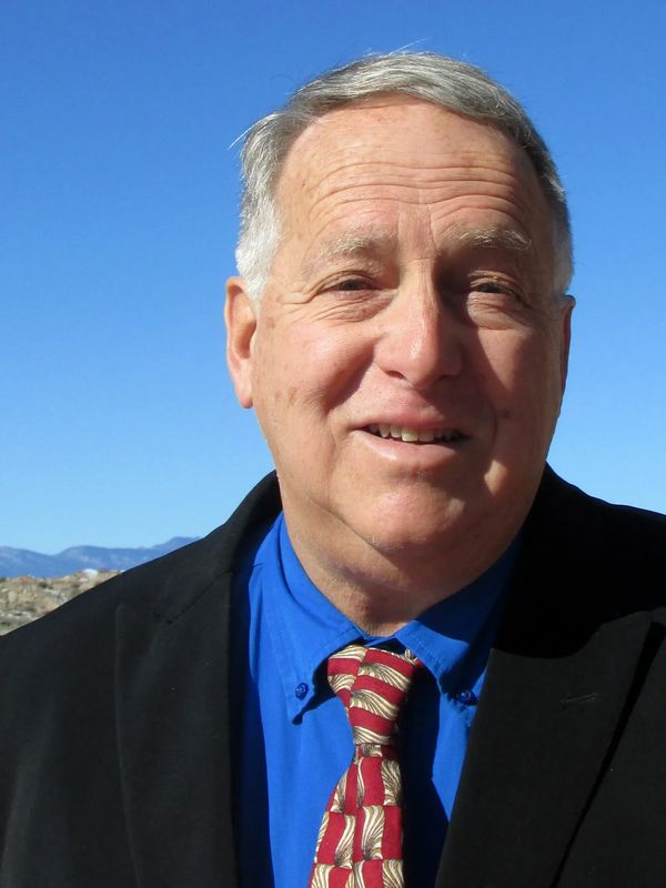 Smiling Carlton Pennington in a blue shirt and patterned tie under a clear blue sky.