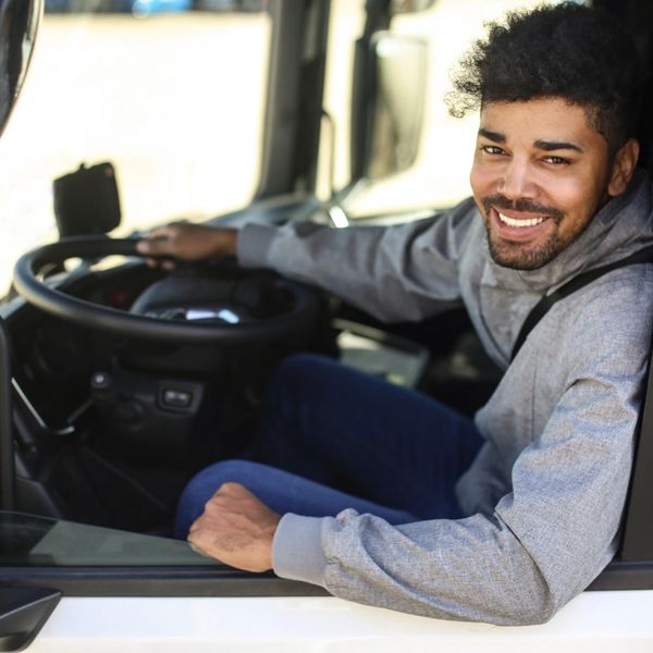 Smiling man sitting in a vehicle driver's seat looking out the window.