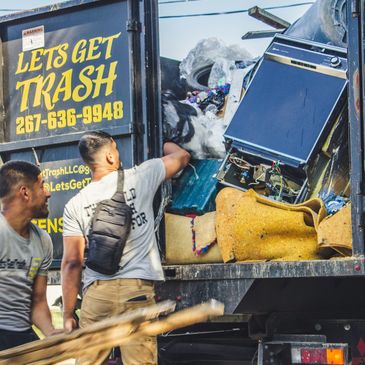 rear of dump truck with lets get trash' employees throwing away construction debris