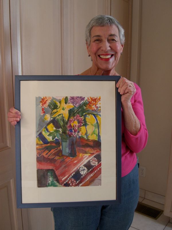 Elderly woman proudly holding floral painting.