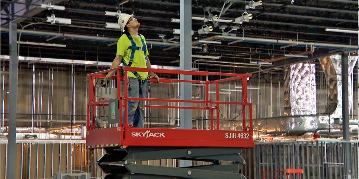 Man operates a scissor lift in an industrial setting, emphasizing OSHA training and safety protocols