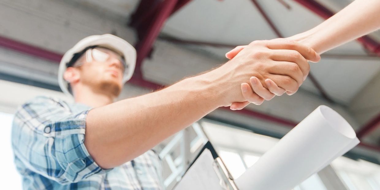 A contractor and client shake hands, finalizing reliable financing options while reviewing a bluepri