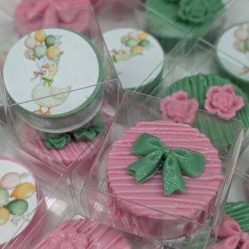 Decorative pink and green cupcakes with bows and floral designs in clear boxes.