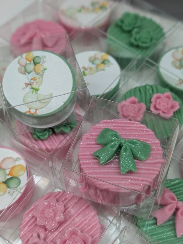 Decorative pink and green frosted cakes with floral and bow designs, packed in clear boxes.