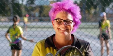 Person with bright purple hair holding a tennis racket.