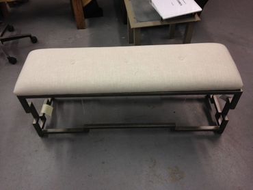 A modern bench with a beige cushioned seat and a metal frame.