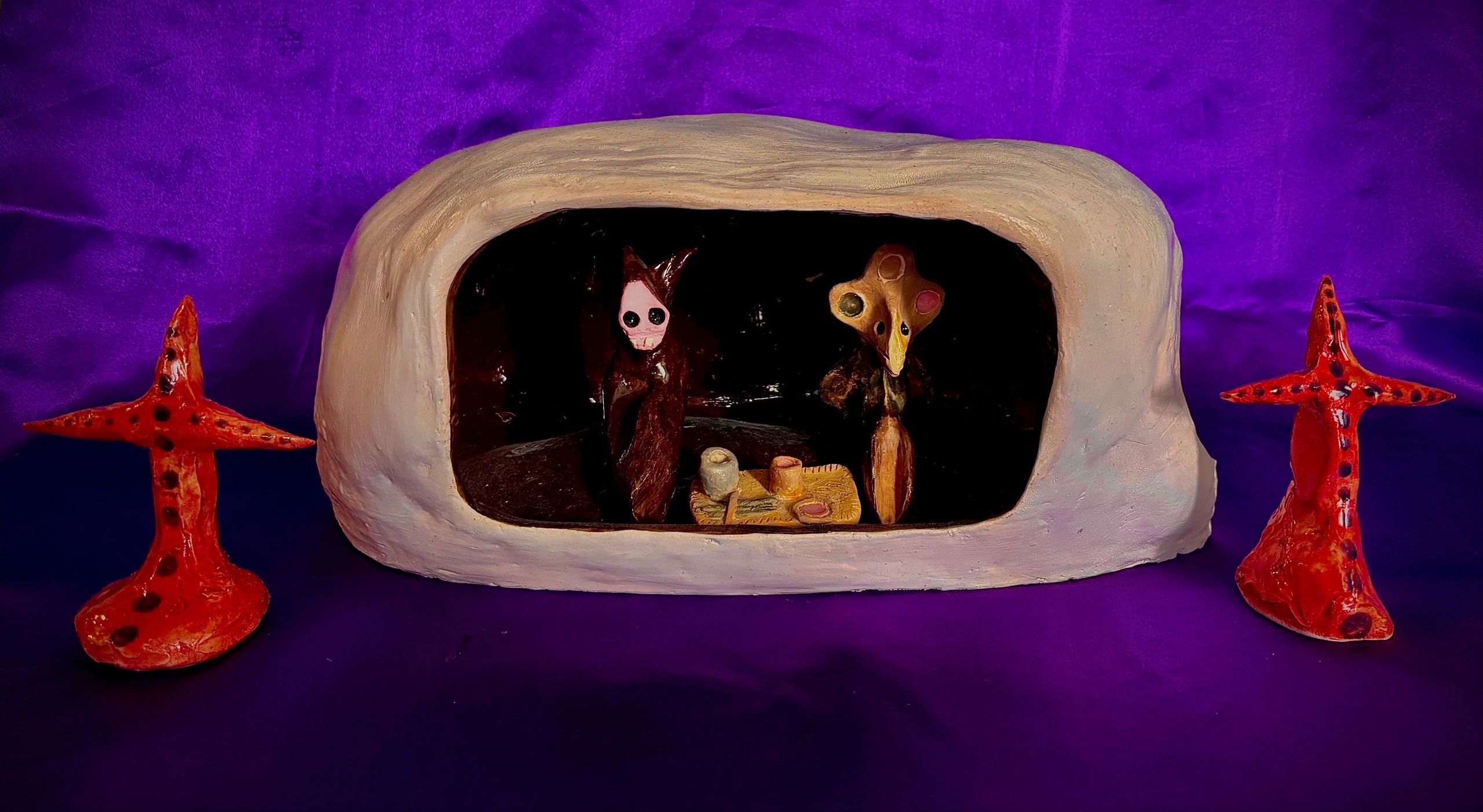 Clay sculpture scene with abstract characters inside an arch and orange starfish figures.