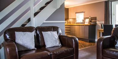 Cozy living room with brown leather sofas and a view into a modern kitchen.