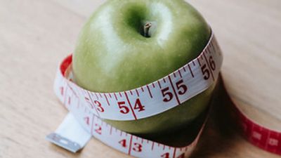 Green apple wrapped with a measuring tape on a wooden surface.