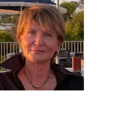 A woman with short hair smiling outdoors during sunset.