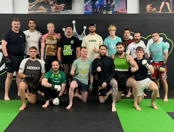 Group of mixed martial artists posing in a gym with gloves and training gear.
