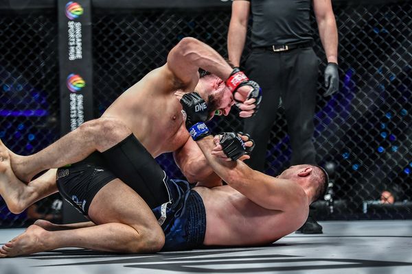 Two mixed martial artists grappling intensely on the mat inside a caged arena.