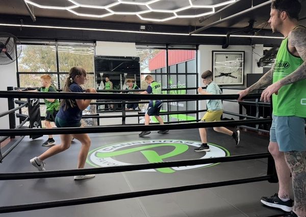 Kids training inside a boxing ring with a coach.