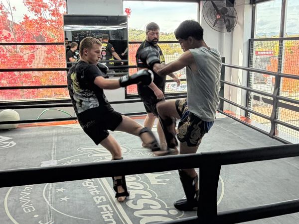 Two fighters sparring in a ring with a coach watching.