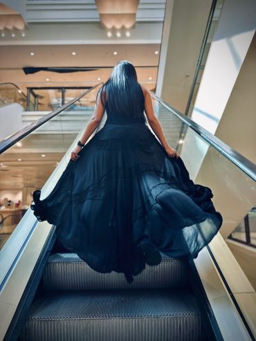 Woman in black dress on escalator.