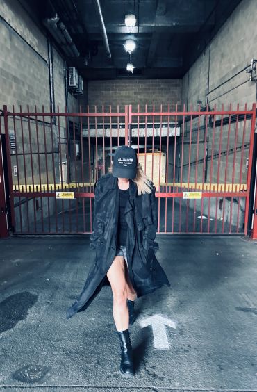 Person in black coat and boots walking in front of a red gate.